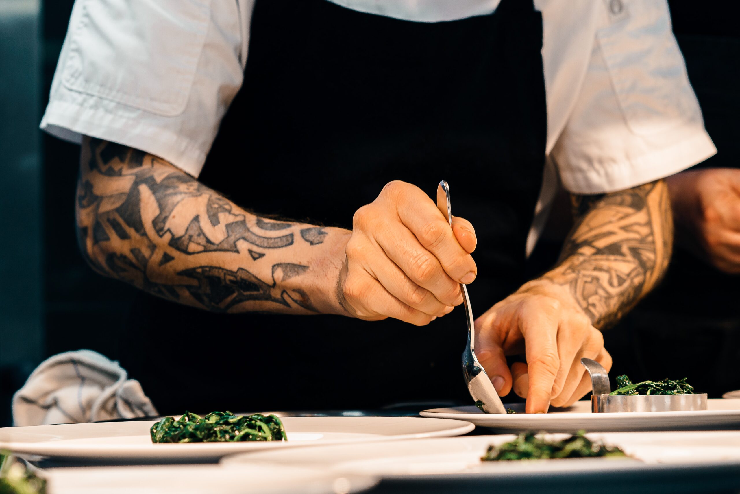 Cook with tattoos plating a dish